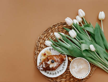 Easter, spring, 8 march, mother day, still life scene. White tulips, croissant and coffee cup on brown background, breakfast sceneの写真素材