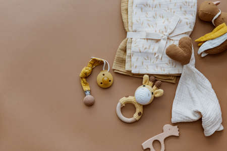 Bib and wooden toys. Set of baby stuff and accessories for newborn on brown background. Baby shower or baby care concept. Fashion newborn. Flat lay, top viewの写真素材