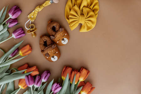 Set of baby shoes, toys, accessories, fresh spring tulips on brown background. Newborn stuff. Flat lay, top viewの写真素材