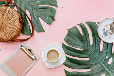 Flat lay women's office desk. Female workspace with clip board, tropical leaves, accessories, cup of coffee on pink background. Top view .Copy spaceの写真素材