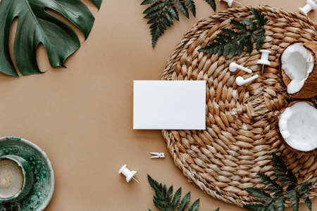 Mock up blank card, flat lay with coffee cup, coconut, green monstera leaf on brown background. Space for text, blogger background, neutral colors, workspaceの写真素材