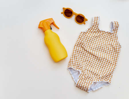 Summer kid's vacation concept - swimsuit with sunscreen cream and sunglasses on neutral background, minimal holiday fashion babyの写真素材