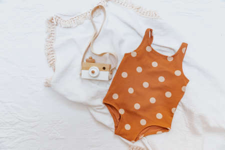 Summer concept. Baby girl swimsuit on white background, ramp leaf and wooden camera toy. Holiday baby conceptの写真素材