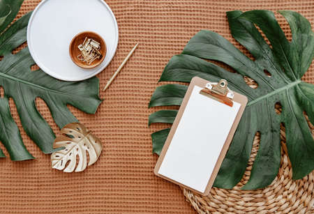 Flat lay office desk table with blank paper clipboard mockup, monstera leaf, office supplies. Modern feminine workspace concept.の写真素材