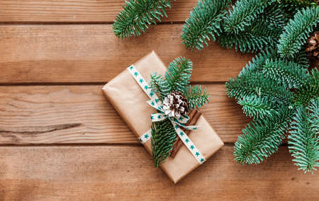 Christmas card template with fir tree branch and gift box on wooden background. Top view flat lay with copy spaceの写真素材