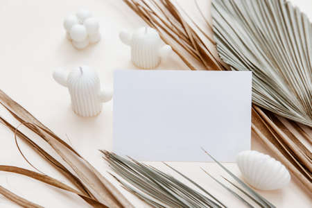 Blank greeting card mockup, dry palm leaf and candles on beige table background. minimal branding, template for wedding in Scandinavian style.の写真素材