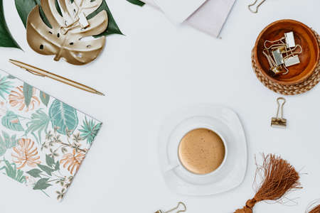 Flat lay Blogger workspace. Home office desk with tropical monstera leaf, cup of coffee, supplies,...