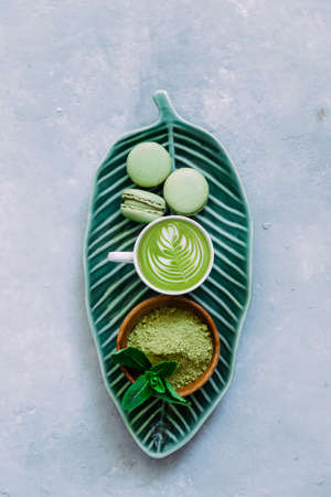 Matcha green latte and macaroons dessert with matcha powder, bamboo whisk and spoon on a blue background. Japanese tea ceremony. Top view, flat lay.の写真素材