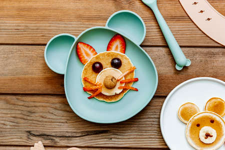 Creative meal for a child, pancake with strawberry, funny food over wooden background. Top view, flat layの写真素材