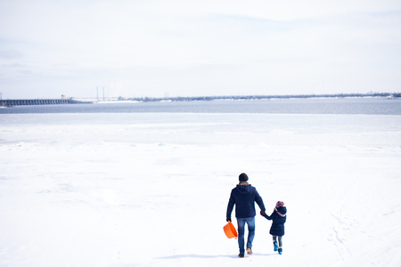 Father with daugther walking on frozen river with panoramic view of horizon and snowy riverの写真素材