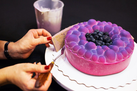 Woman's hands decorating mousse blueberry cake on black background