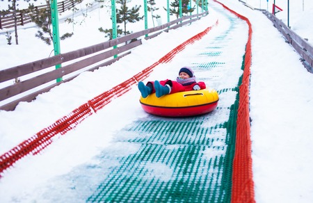 Little girl sliding down the hill by tubing, snow aroungの写真素材