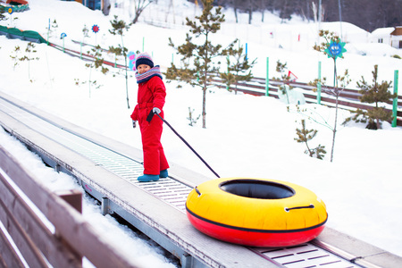 Little smiling girl in red overall is going up with her tubing using liftの写真素材