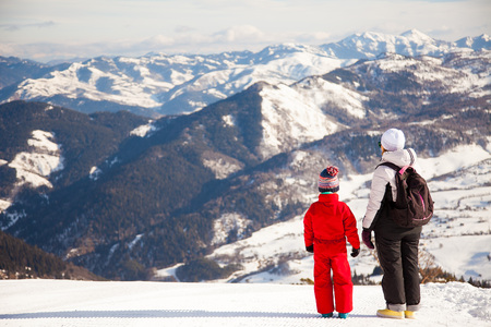 Happy family in winter clothing at the ski resort, winter time, watching at mountains in front of themの写真素材