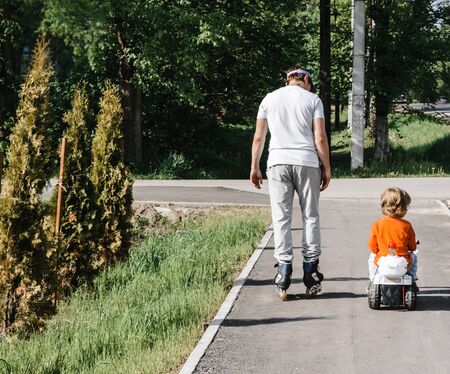 father and son for a walk. boy on a toy children motorcycle dad roller skate. family holiday. father dayの写真素材
