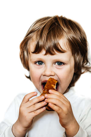 the child is smiling and eating a piece of cake. the boy loves homemade sweets and pastries. White backgroundの写真素材