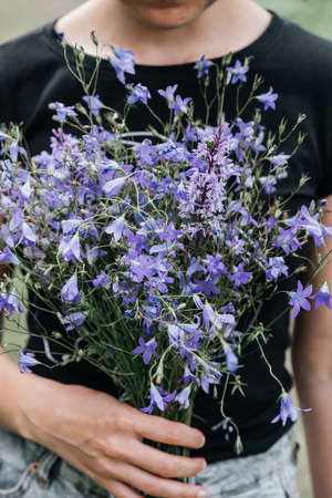 young woman with long hair holds in her hands a bouquet of wildflowers of blue color. rural meadows,...