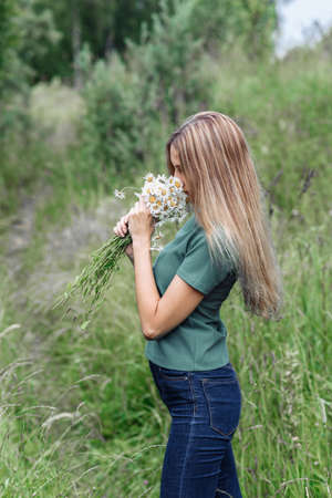 young woman with a wreath of daisies on her head in the sun on a field of grassの写真素材