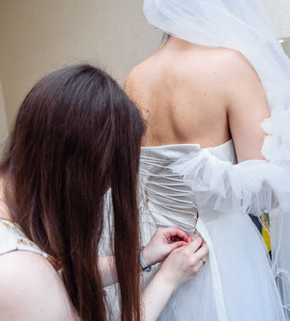 gathering the bride wedding preparation bridesmaid helps to put on a dress with a corset and lacingの写真素材