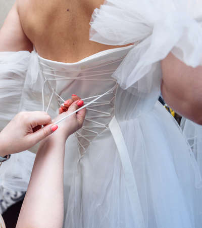gathering the bride wedding preparation bridesmaid helps to put on a dress with a corset and lacing