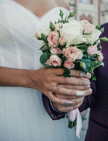 brides hand with an elegant wedding ring with white gold diamonds on a bouquet of their peoniesの写真素材
