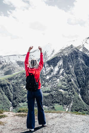 young woman stands with her back with a backpack on the observation deck overlooking the mountainsの写真素材
