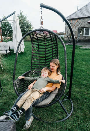 mother and child ride on a wicker rattan cocoon swing. son shakes a woman, shakes a summer vacation in natureの写真素材
