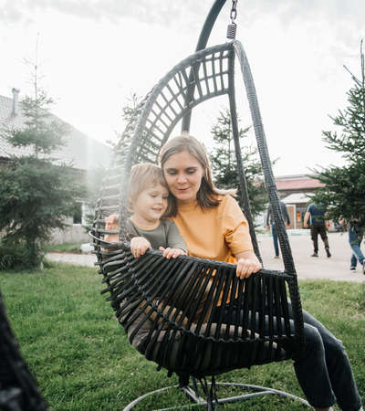 mother and child ride on a wicker rattan cocoon swing. son shakes a woman, shakes a summer vacation in natureの写真素材