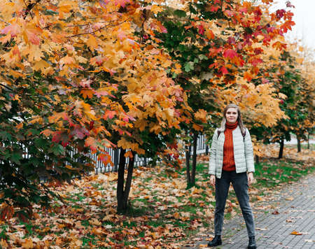 young woman autumn landscape red yellow maple leaves, in an orange knitted warm sweater
