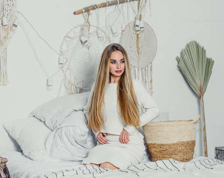 young woman with long luxurious blond blonde hair on the bed in the bedroom in white tones interior. sexyの写真素材