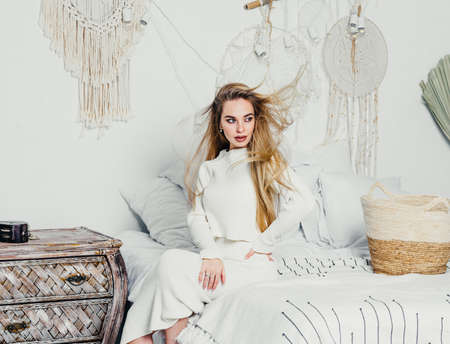 young woman with long luxurious blond blonde hair on the bed in the bedroom in white tones interior....
