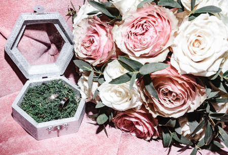 white gold wedding rings in a box and a bridal bouquet of delicate roses and greenery