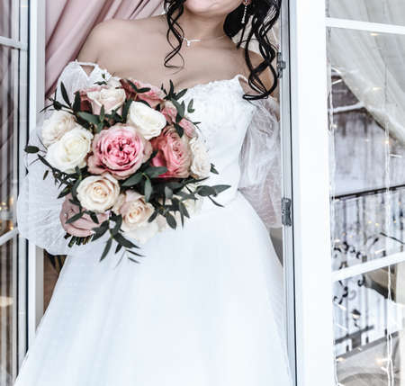 young beautiful bride in a white delicate elegant airy wedding dress with a bouquet of flowers roseの写真素材