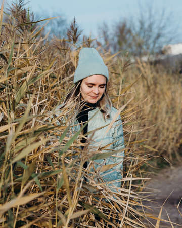 Back view of stylish girl in beige coat and hat against the background of dry reeds and blue sky.の写真素材