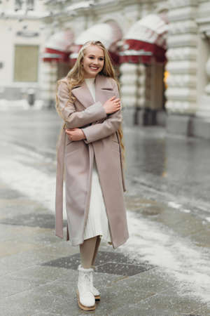 beautiful young caucasian smiling woman in beige coat with long hair walking outdoors,の写真素材