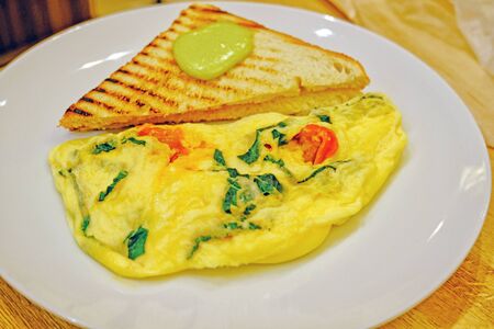 scrambled eggs omelette with fresh herbs tomatoes, basil, greek cheese, parmesan, toast and oregano and garlic panini toasts closeup viewの写真素材
