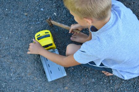 Little boy breaks an old toy the car the hammer. Top view. Boy beats a toy