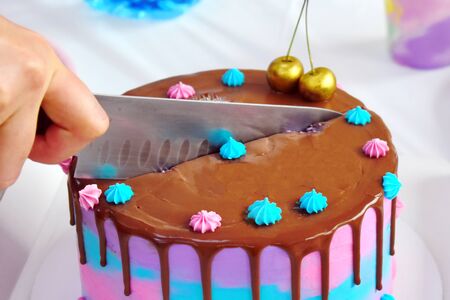 Hand with a knife cuts a colorful cake.
