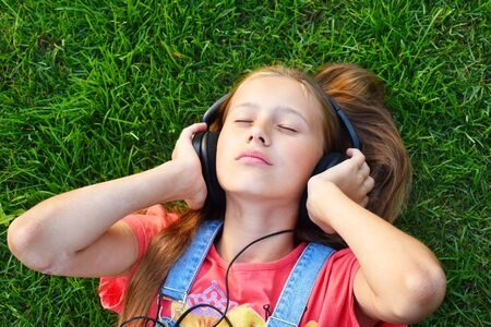 Child girl in big headphones enjoys the music. Teen girl listens to a cheerful tune.の写真素材