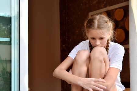 A young girl sits on the windowsill of an open window.の写真素材