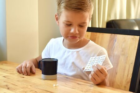 Boy child sitting at a table with medicines. Seasonal flu and colds. Prevention of childhood diseases.の写真素材