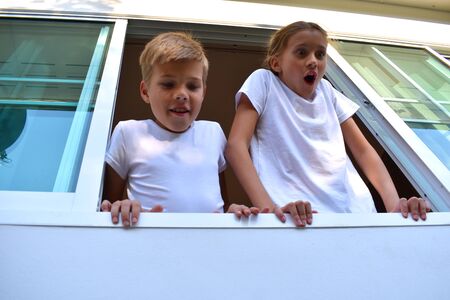 Brother and sister looked out the open window. Cute children in the window look down.の写真素材