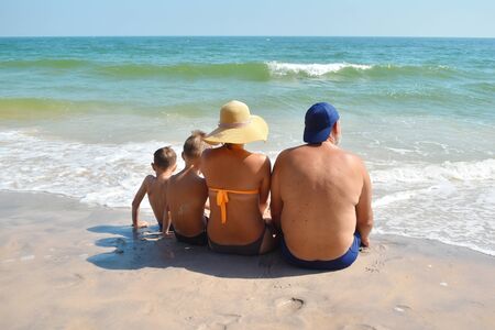 Family sitting on the sand on the beach. Family holidays by the sea. Happy children and parents on vacation in the tropics.の写真素材
