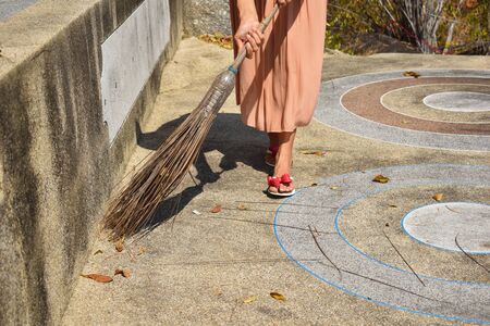 A woman sweeps away leaves autdoor. Woman sweeping in the summer plot.の写真素材
