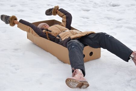 Girl in a cardboard box on hill in winter. Child to have fun in winter. Winter is funny game....