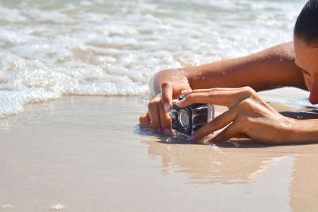 Mini camera on the beach in the sand. Photographing the sea. Girl takes off on cameraのeditorial素材