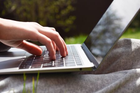 Girl with laptop on green grass. Remote schooling. The child works at the computerの写真素材