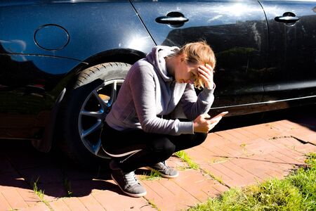 A depressed woman is sitting by an expensive car. The car will not startの写真素材