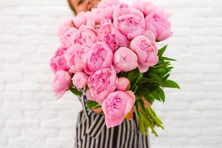 a young girl with pleasure holds in her hands pink peonies bouquet.の写真素材