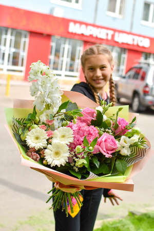 Girl child gives flowers. Women's Day. Teenage with flowers outside a storeのeditorial素材